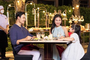 A dining table set outdoors with a waiter, a man, a woman, and a child.