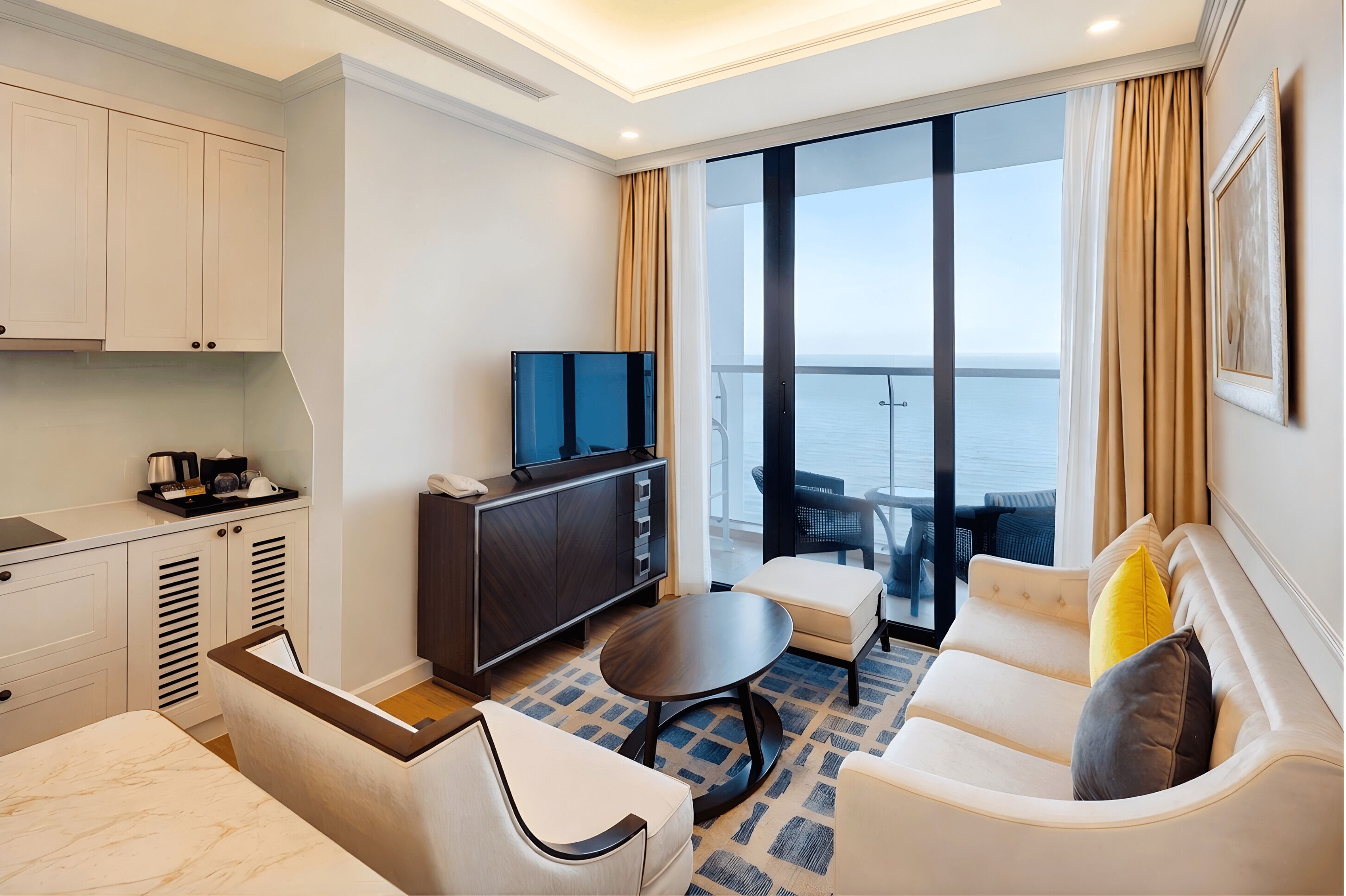 Una habitación de hotel moderna con balcón, una televisión de pantalla plana, un sofá, una mesa de comedor y una zona de cocina.