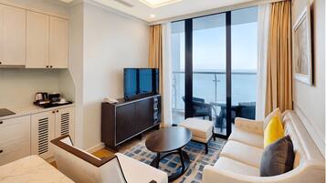 Una habitación de hotel moderna con balcón, una televisión de pantalla plana, un sofá, una mesa de comedor y una zona de cocina.
