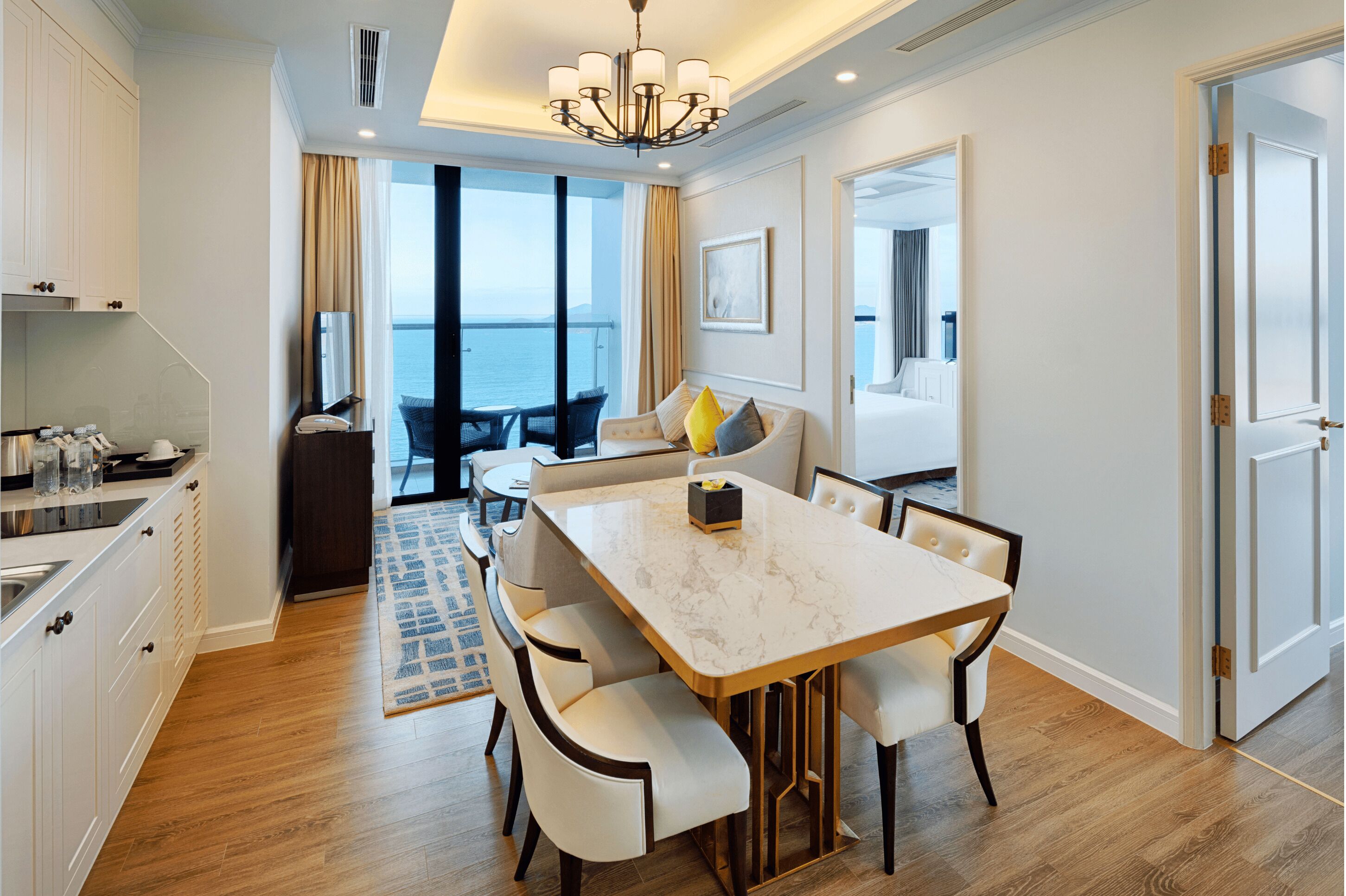 A modern hotel room with a dining area, a balcony with a view of the sea, and a large window.