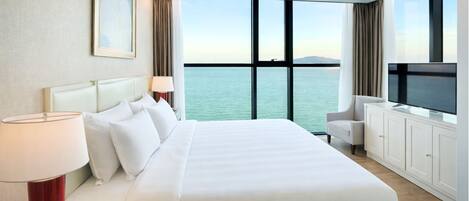 A hotel room with a bed, a TV, a desk, and a view of the sea.