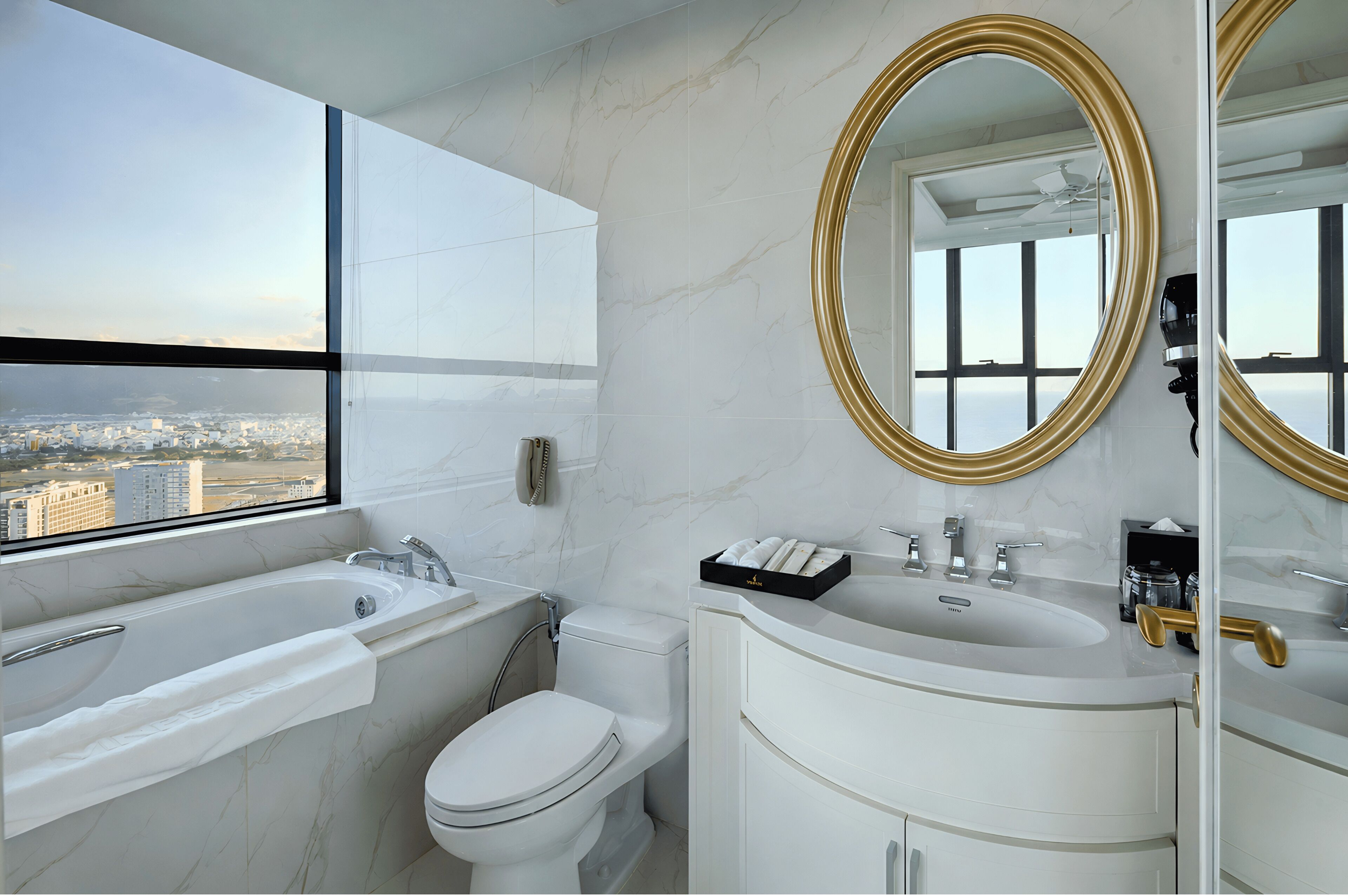 A modern bathroom with a bathtub, toilet, and vanity, featuring marble walls and large mirrors.