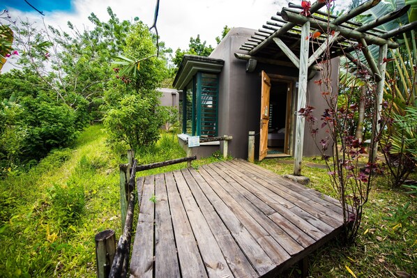 A wooden deck leading to a building with a green door, surrounded by lush greenery. - L'Exil Lodges (Riviere des Anguilles)