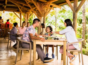 A wooden outdoor dining area with tables and chairs, surrounded by greenery. - L'Exil Lodges (Riviere des Anguilles)