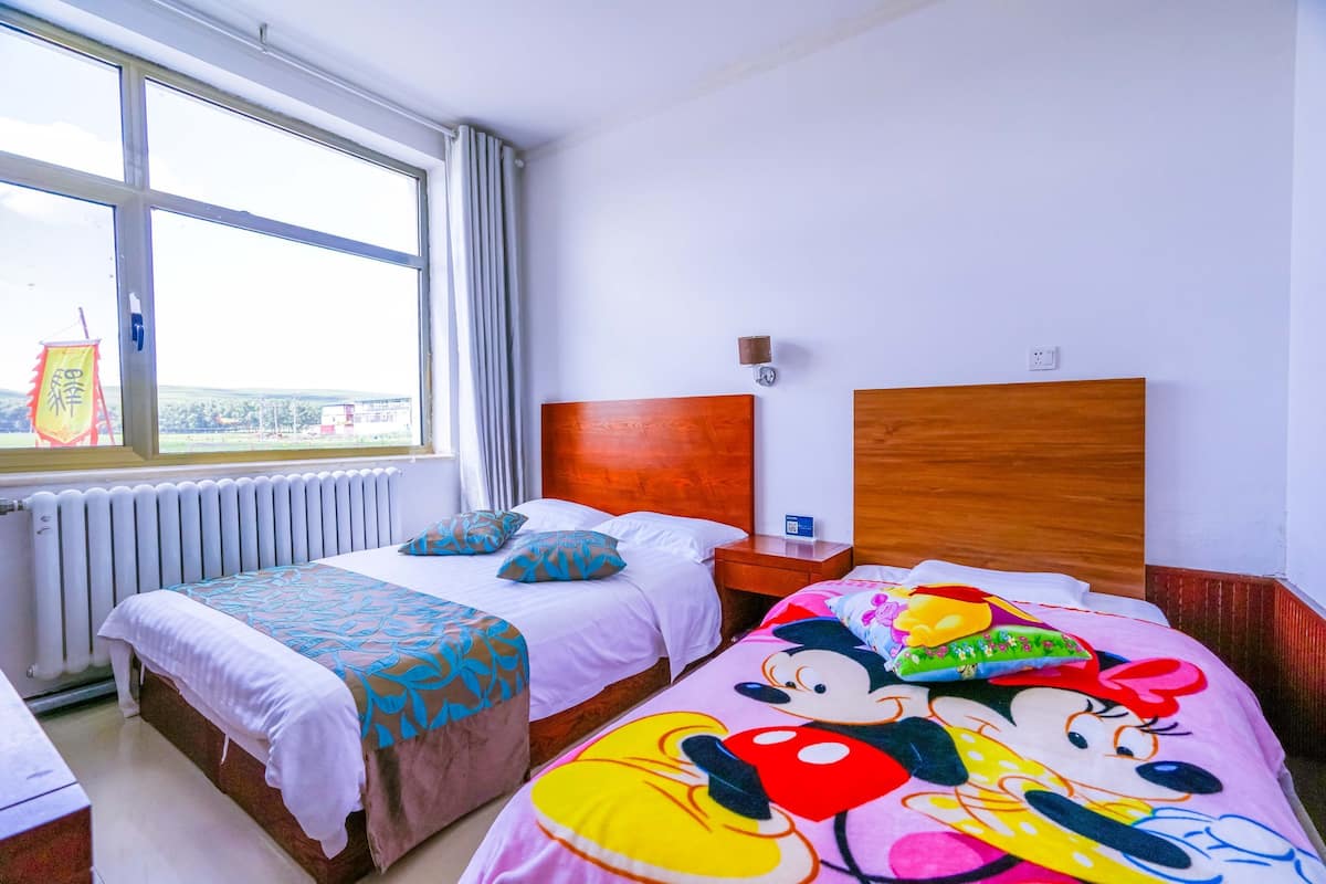 Une chambre d’hôtel avec deux lits, une fenêtre avec des rideaux, une tête de lit en bois et une table de chevet avec une horloge.