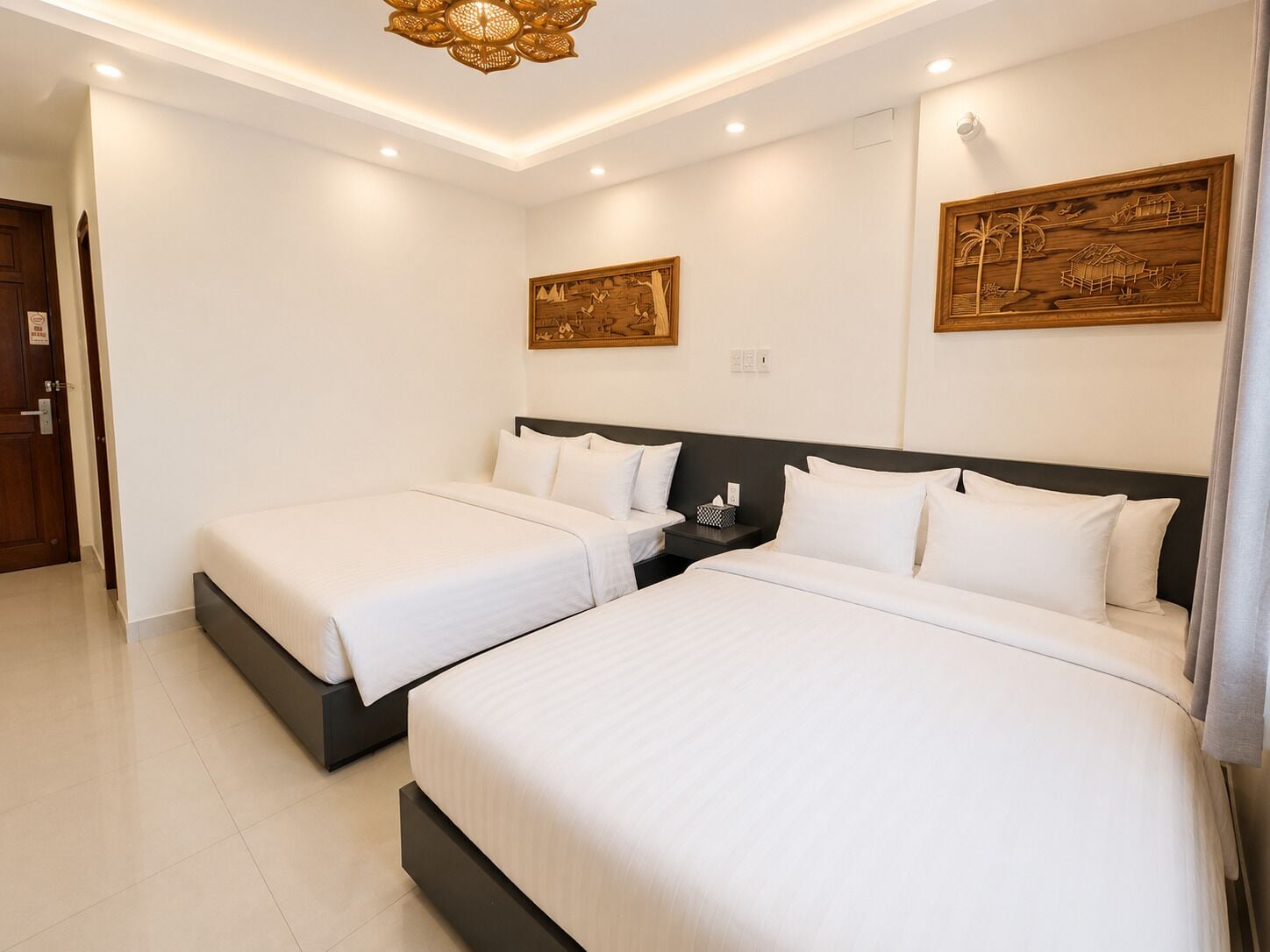 A hotel room with two beds, a dark headboard, a wall-mounted artwork, and a ceiling light fixture.