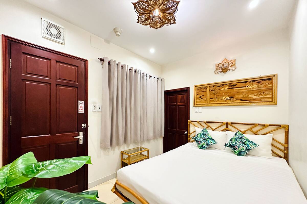 Ein Hotelzimmer mit einem Bett, einem Holz-Kopfteil, einem Wandbild, einem kleinen Tisch und einer großen Zimmerpflanze.