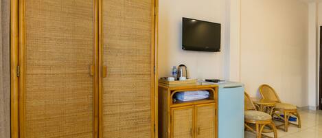 Ein Zimmer mit großem Holzschrank, Wandfernseher, kleinem Tischchen mit Wasserkocher und zwei Korbstühlen.
