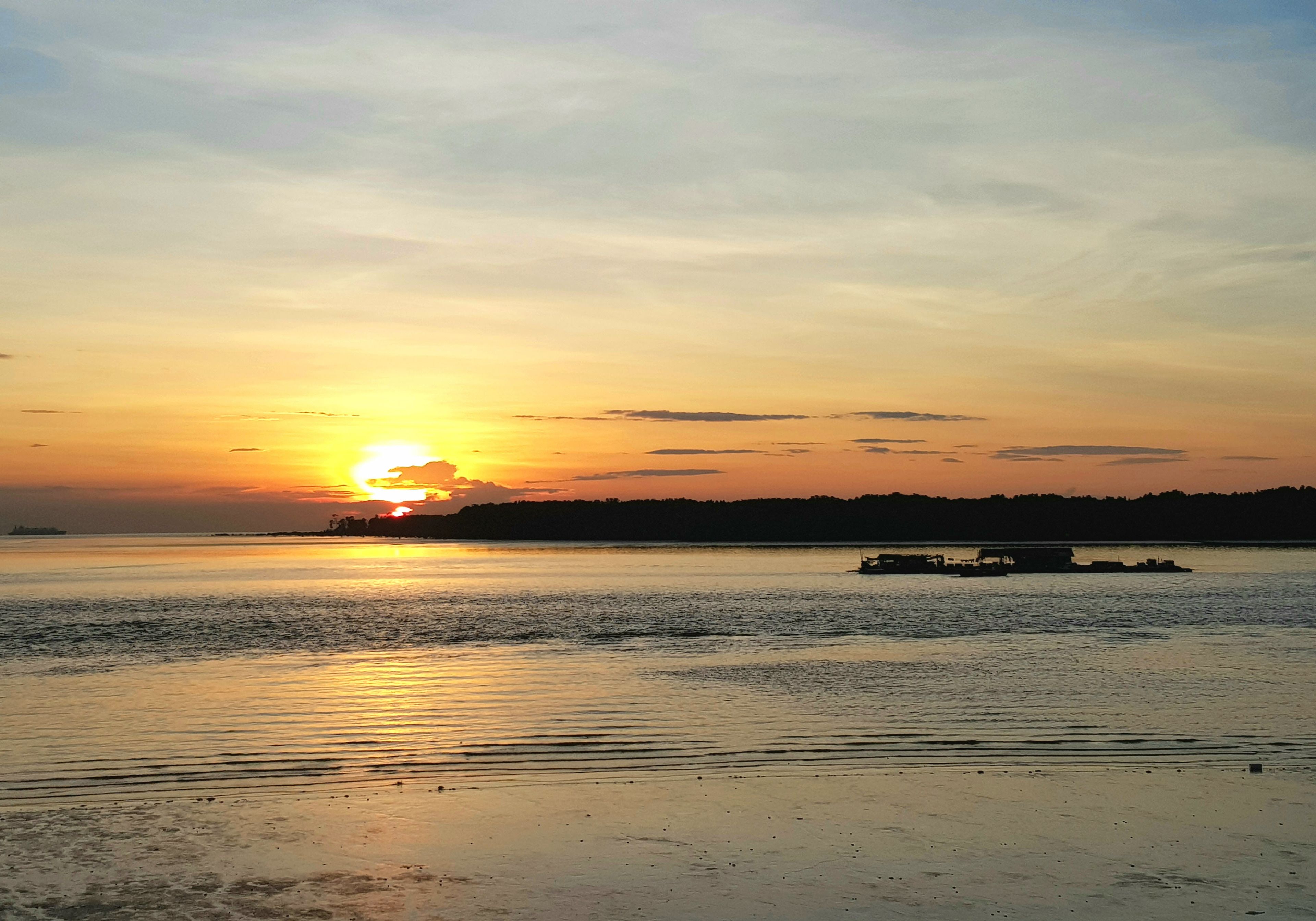 Een zonsondergang boven kalm water, met een boot op de voorgrond.
