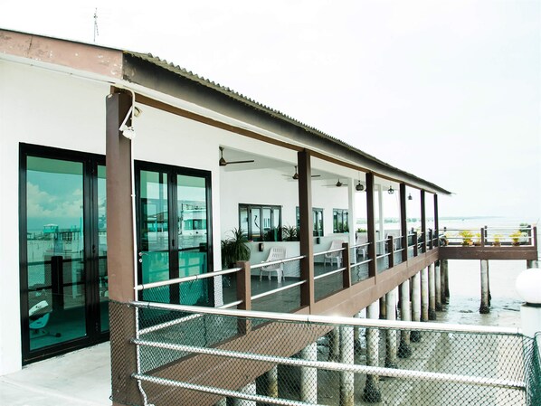 A modern building with a covered outdoor area featuring a seating area with chairs and tables, large windows, and a view of the water. - Kukup Xiang Holiday Home (Kukup)
