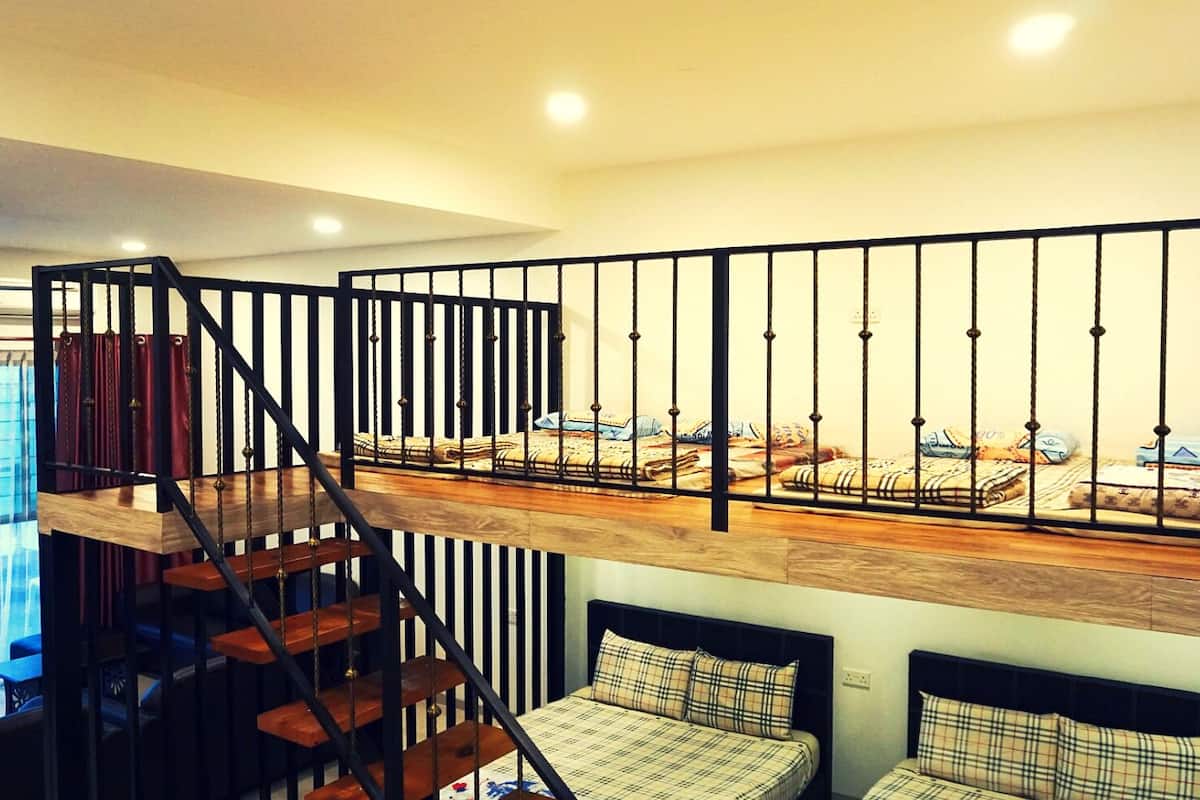 A loft-style bedroom with a wooden platform bed, a black metal railing, and a staircase.