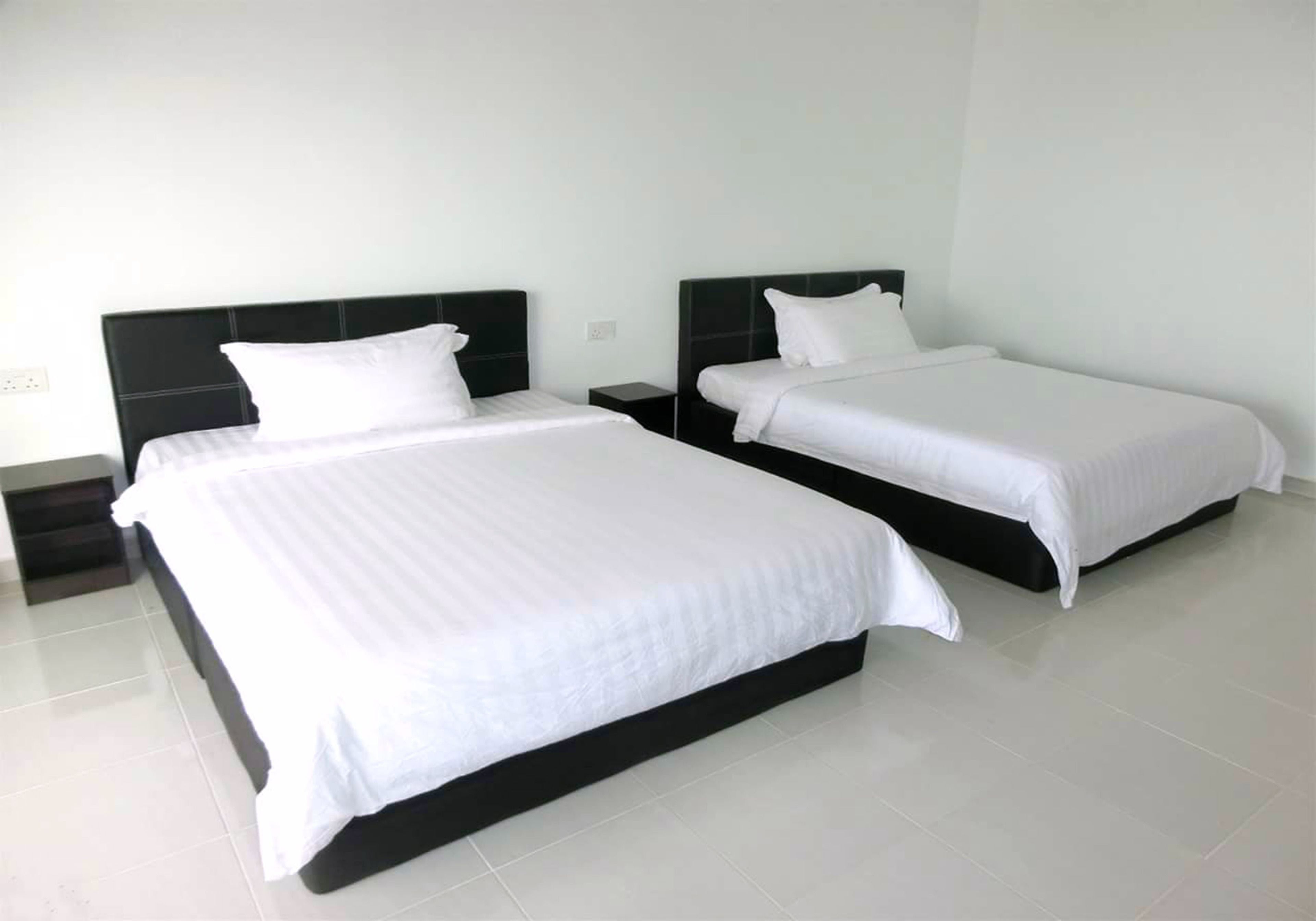 Duas camas de solteiro com cabeceiras pretas num quarto com paredes brancas e chão de azulejos.
