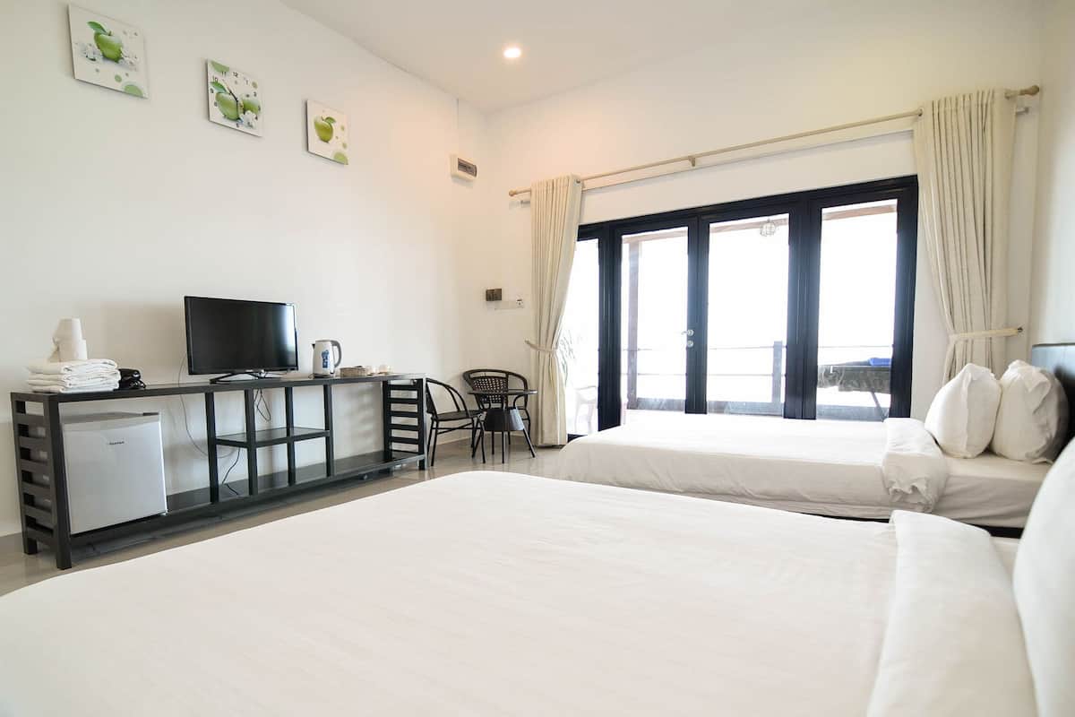 A hotel room with two beds, a desk with a TV, a small refrigerator, and a window with curtains.