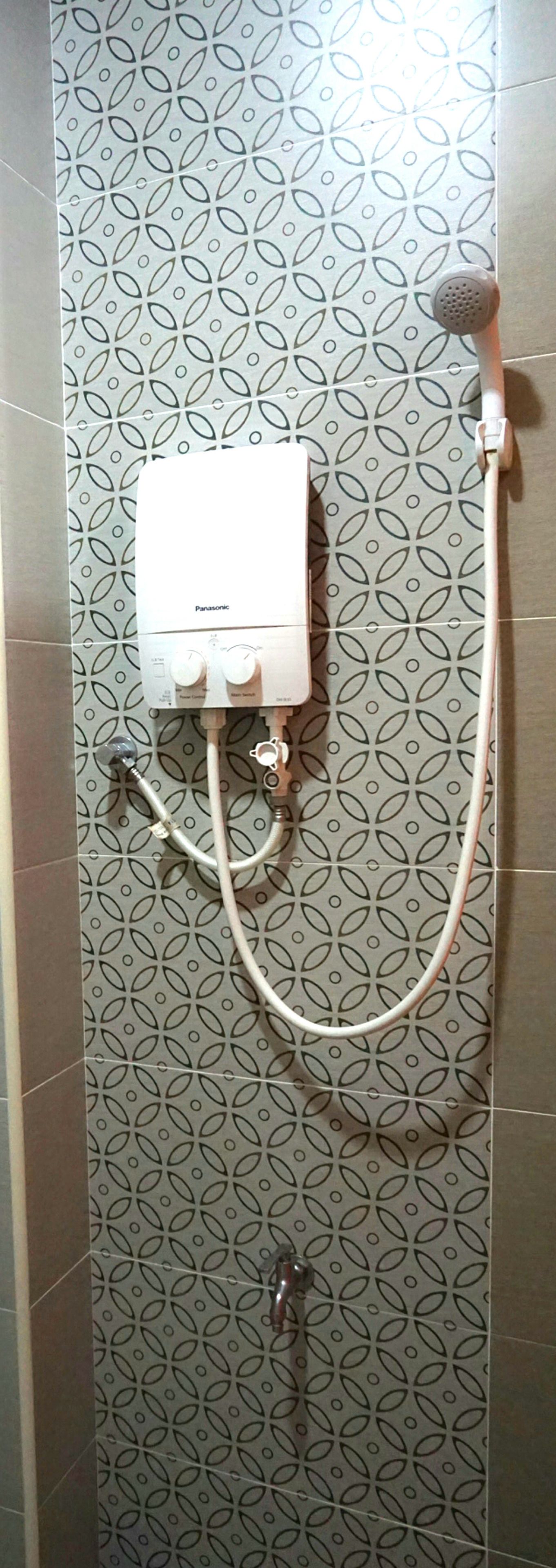 A bathroom with a shower unit mounted on a wall with a geometric tile pattern.
