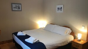 A neatly made bed with white linens and a dark blue bedspread, two folded towels on the bed, and a bedside table with a lamp. - Tully Mill Cottages (Enniskillen)