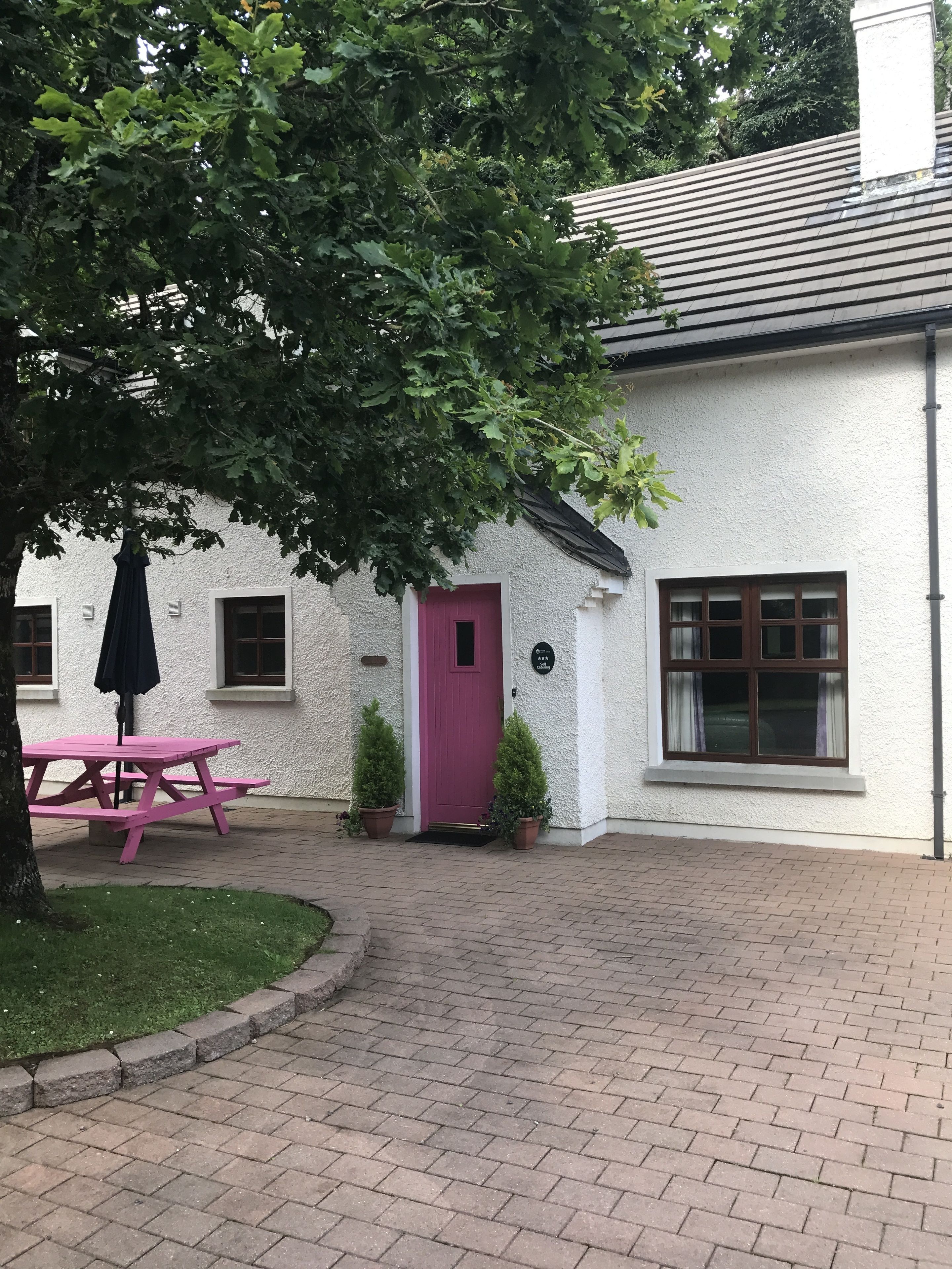 A white building with a pink door, a picnic table, and potted plants.