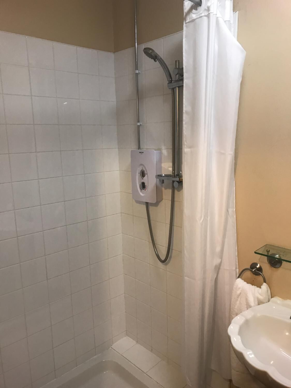A shower with a handheld showerhead and a wall-mounted control panel.