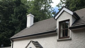 A two-story house with a white exterior, a wooden door, and a small porch area with a bench and potted plants. - Tully Mill Cottages (Enniskillen)