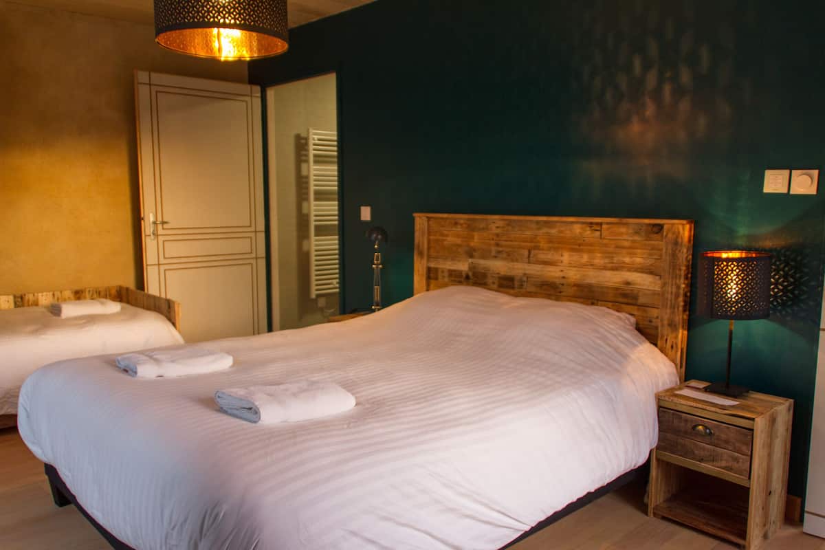 Une chambre avec deux lits, une tête de lit en bois, une table de chevet avec une lampe et une porte donnant sur une salle de bain.