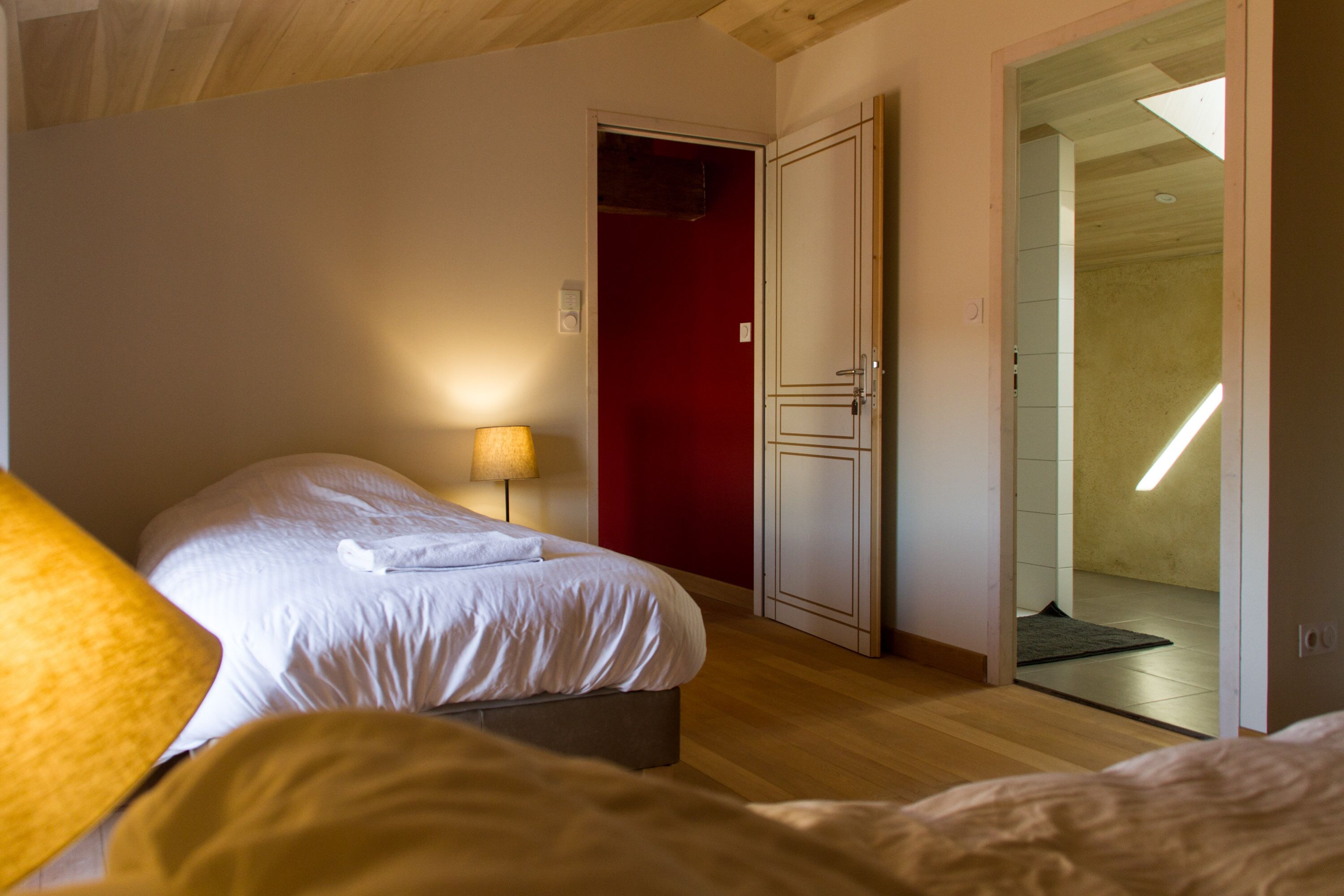 Un dormitorio con cama, lámpara de noche, armario y puerta que da a otra habitación.