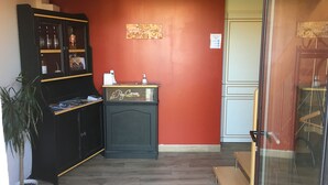 A reception area with a black cabinet, a small desk with a sign, a potted plant, and a red wall. - Le Puy Carmin - Chambres D'hôtes (Bazoges-en-Paillers)