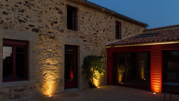 A stone building with a tiled roof, large windows, and a small garden area with a tree. - Le Puy Carmin - Chambres D'hôtes (Bazoges-en-Paillers)