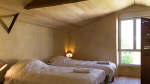 A bedroom with two beds, a nightstand, a wall-mounted lamp, and a window with a view of greenery. - Le Puy Carmin - Chambres D'hôtes (Bazoges-en-Paillers)
