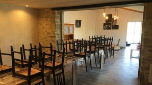 A dining area with multiple wooden tables and chairs, stone walls, and a wooden floor. - Le Puy Carmin - Chambres D'hôtes (Bazoges-en-Paillers)