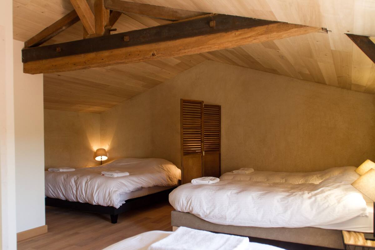 Une chambre avec deux lits, des poutres apparentes, une applique murale et une armoire en bois.