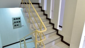 A staircase with yellow handrails, white walls, and a light-colored floor. - CK Residence (Pattaya)