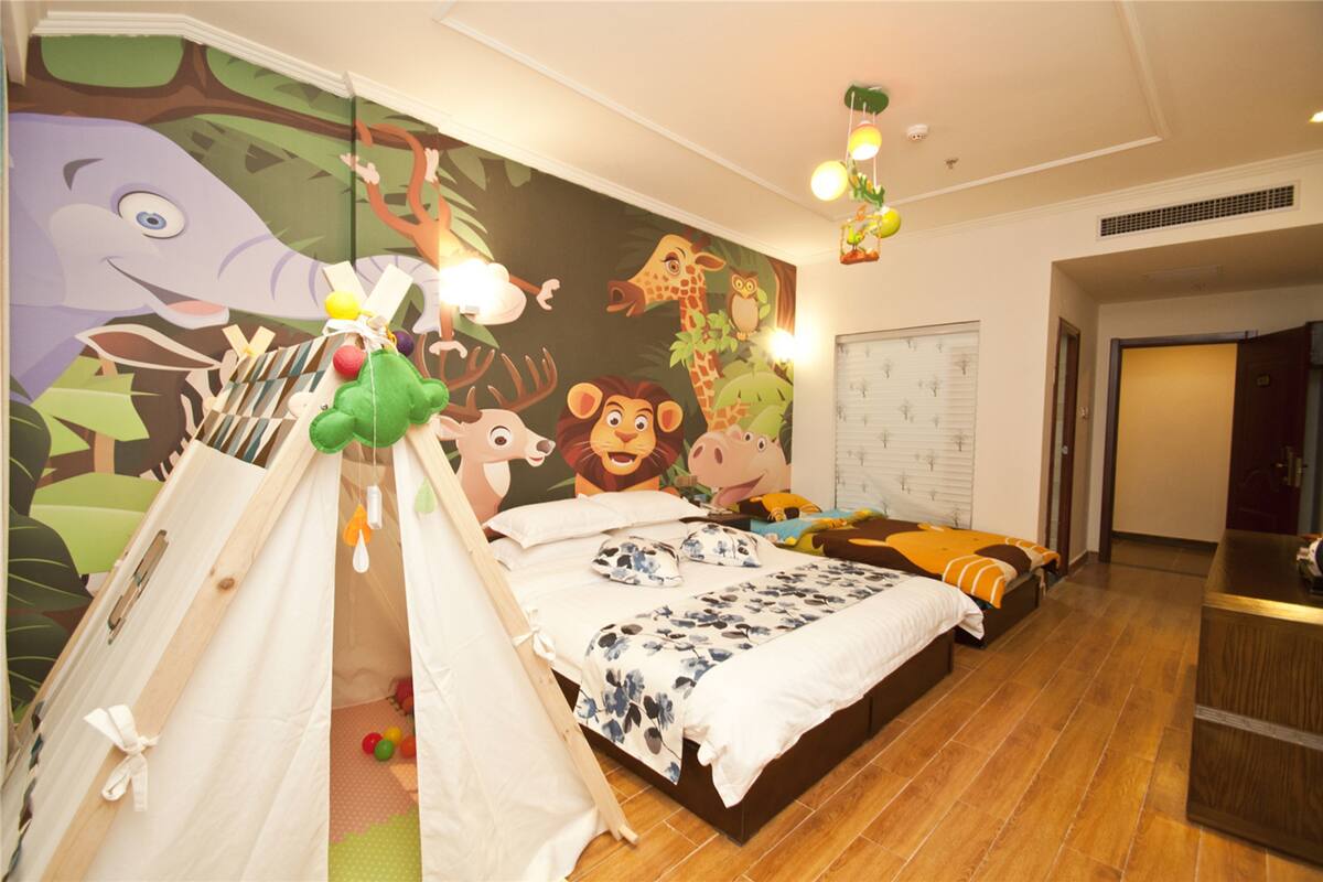 Quarto com um grande mural, um espaço de brincar tipo tenda, cama com várias almofadas e mesa de cabeceira.