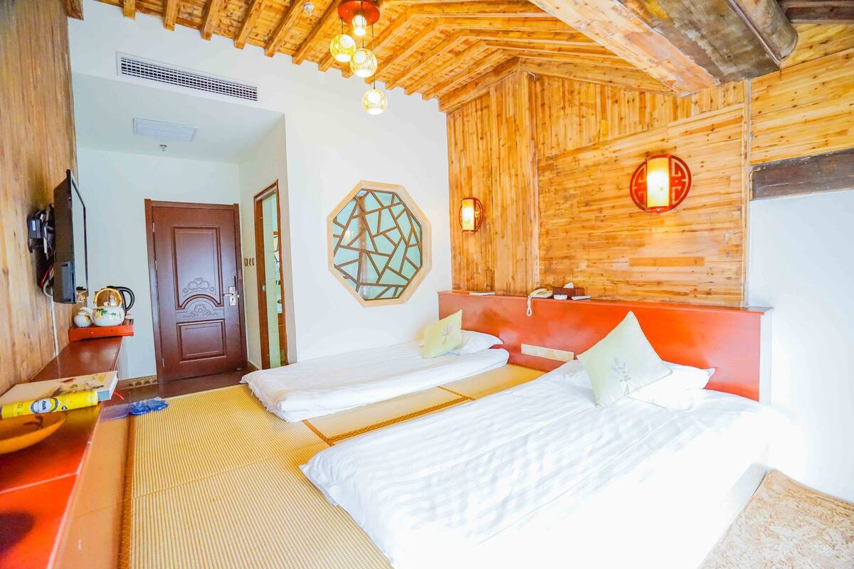 Quarto com duas camas, teto de madeira e luminária fixada na parede.