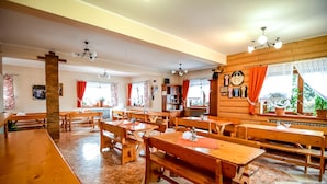 Un vaste espace dédié à la salle à manger, avec des tables et des bancs en bois, de grandes fenêtres dotées de rideaux et un mur en bois orné d’une horloge.