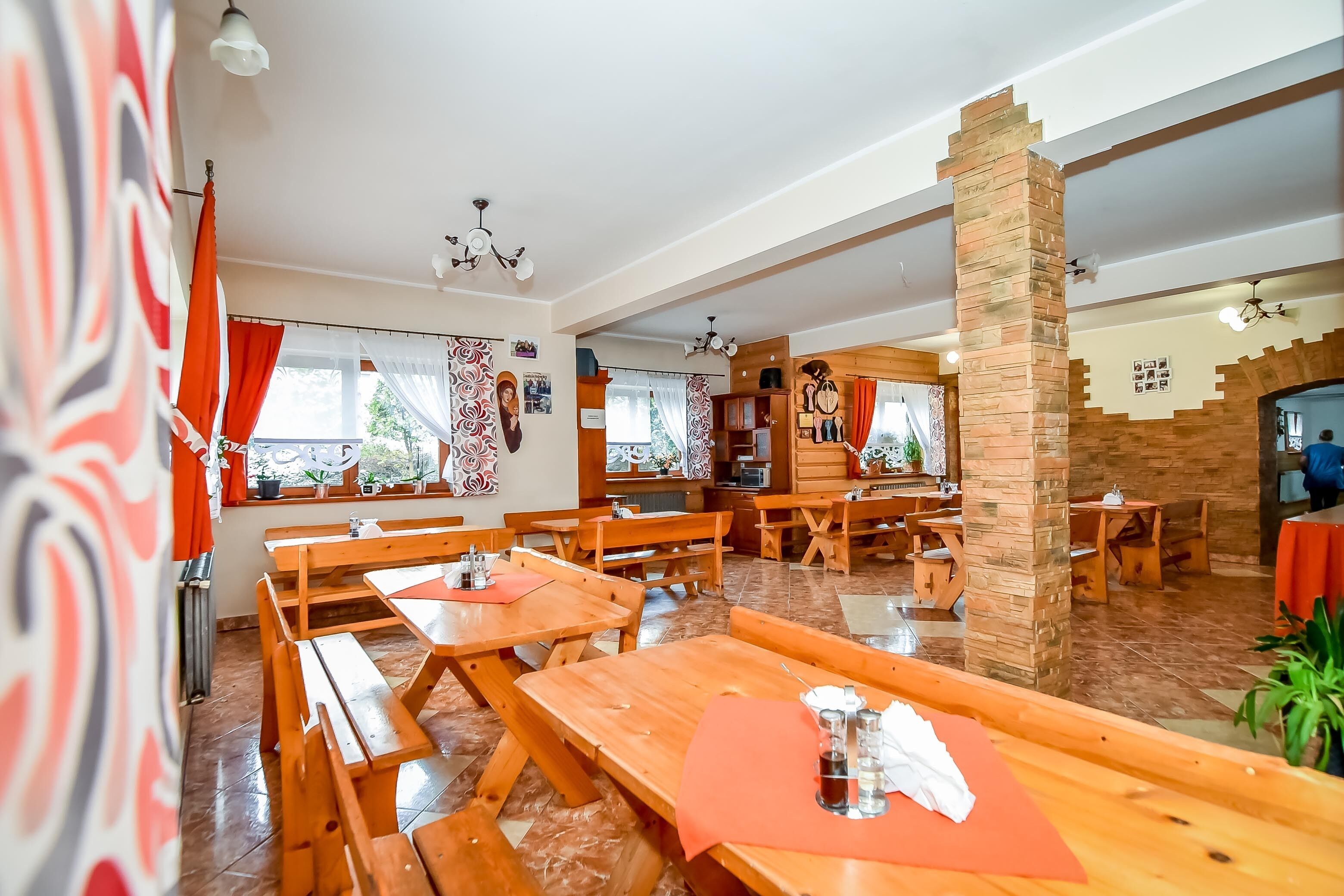 Restaurante com mesas e bancos de madeira, um pilar de pedra e vista para o exterior.
