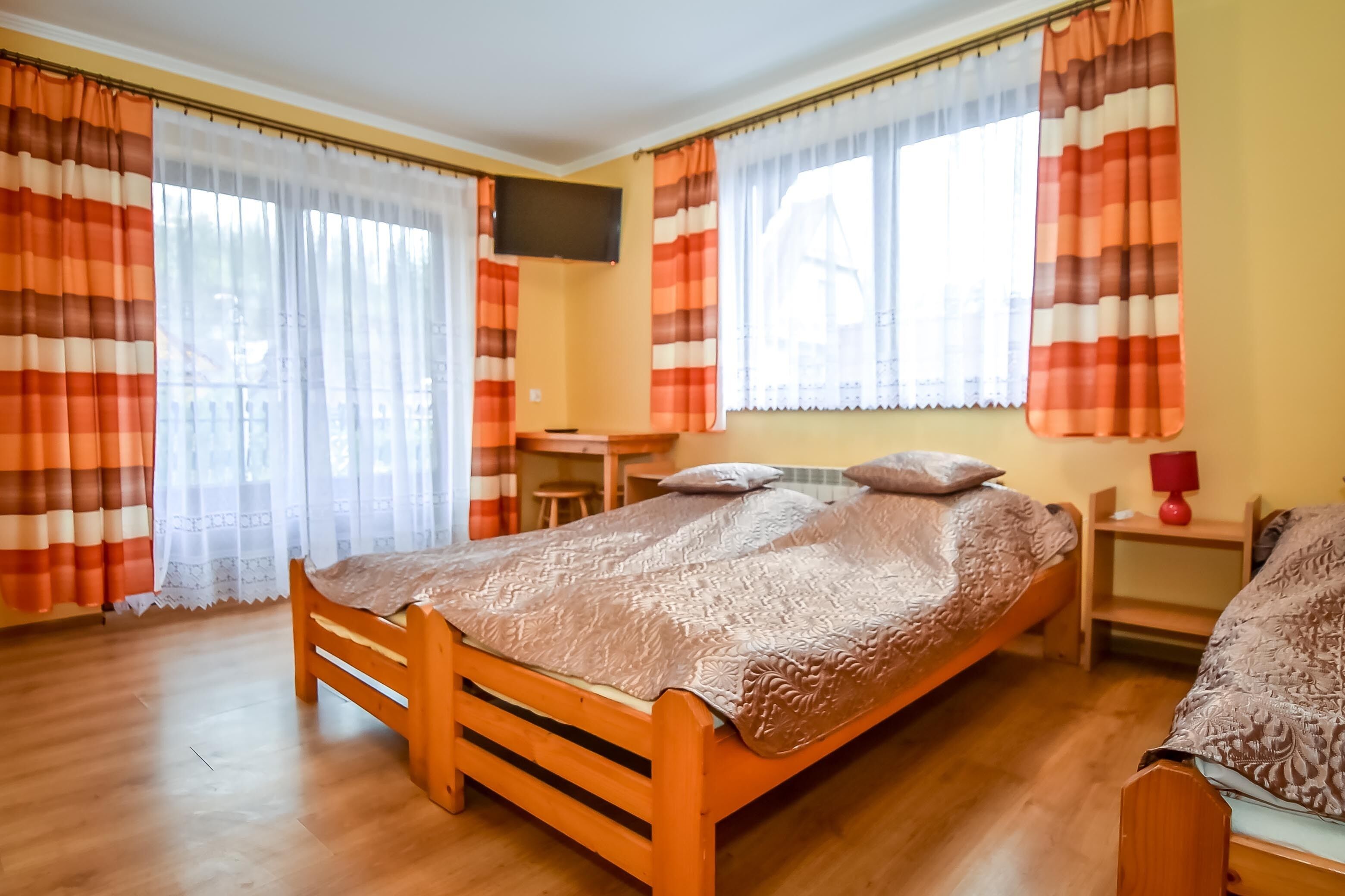 Een slaapkamer met een houten bed, een bureau, een stoel, een televisie en gordijnen.