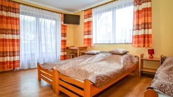 Een slaapkamer met een houten bed, een bureau, een stoel, een televisie en gordijnen.