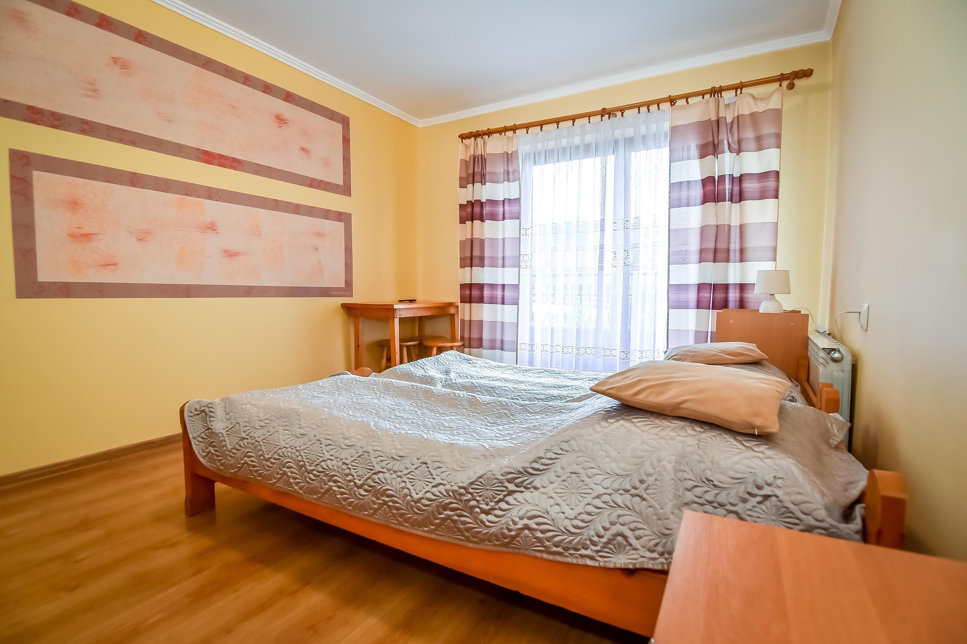 Un dormitorio con cama, mesita de noche, lámpara y cortinas.