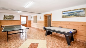 Une pièce avec une table de ping-pong, une table de billard, des murs en bois et un tableau.