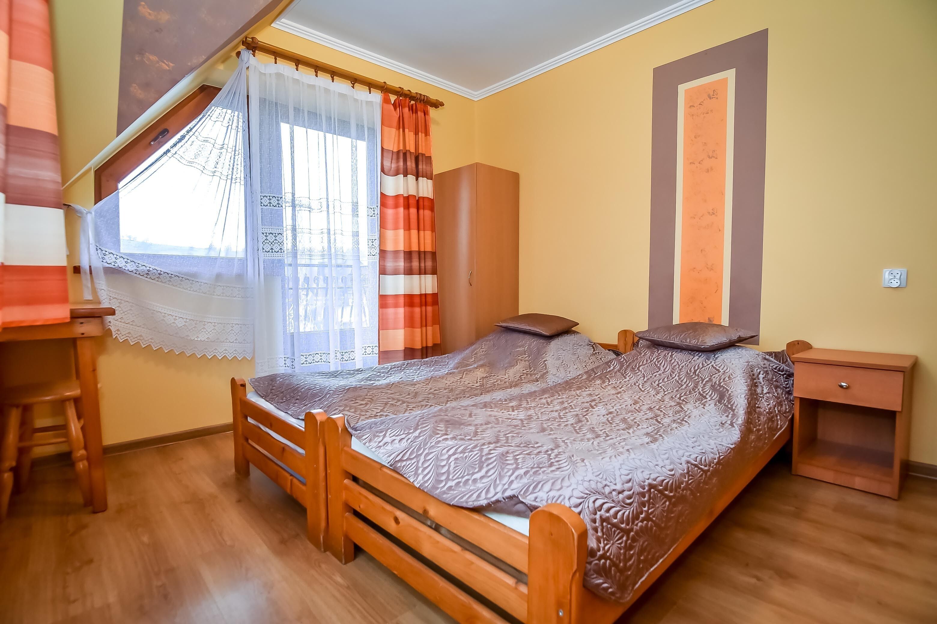 Ein Schlafzimmer mit einem hölzernen Bett, einem Nachttisch, einem Kleiderschrank und einem Fenster mit Vorhängen.