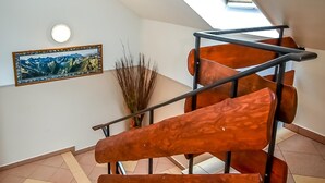 Un escalier moderne avec une lucarne, un tableau représentant un paysage encadré et un grand vase contenant des plantes séchées.