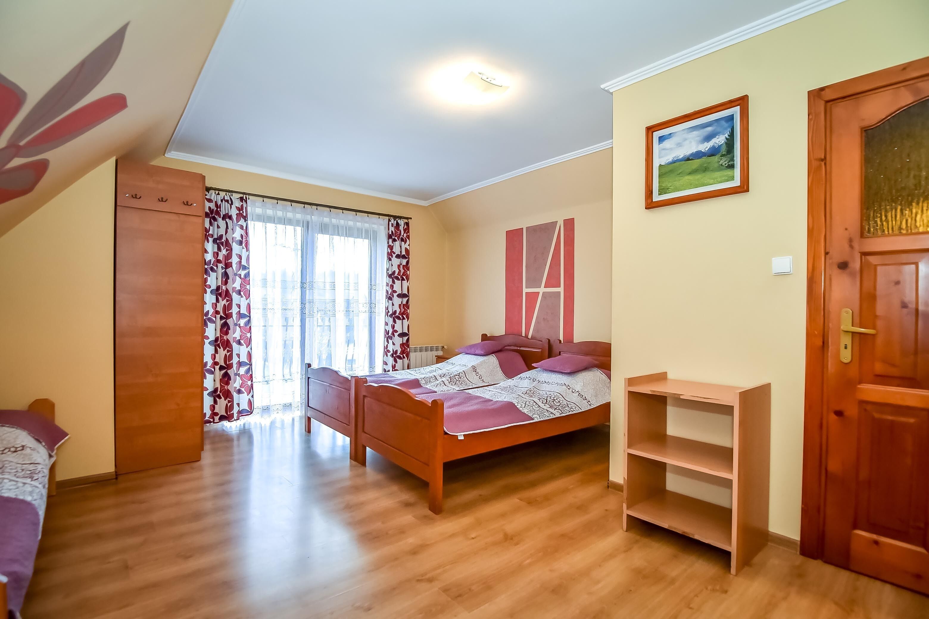 Ein Schlafzimmer mit einem hölzernen Bett, einem Kleiderschrank, einem Fenster mit Vorhängen und einer Tür.