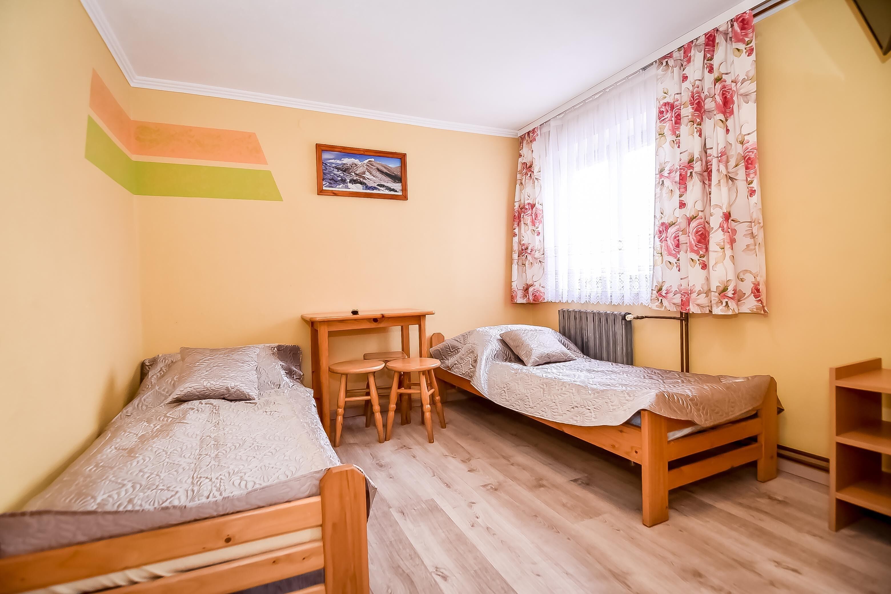 A dormitory room with two wooden beds, a desk, and a chair.