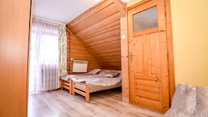 Une petite pièce agréable, avec un plafond en pente, un lit simple, une porte en bois et une fenêtre ornée de rideaux légers.