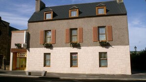 Un edificio de dos pisos con fachada de ladrillo, múltiples ventanas con contraventanas y jardineras en el segundo piso.