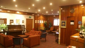 Un hall de hotel con un piano, asientos cómodos, un mostrador de recepción y un área de registro.
