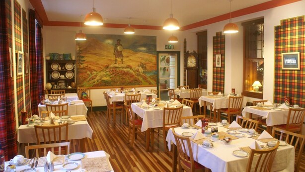 Un restaurante con varias mesas preparadas para comer, un mural en la pared y cortinas de estampado escocés.