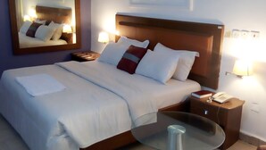 Una camera d'albergo con un letto grande, lampade sui comodini, un tavolino in vetro e una poltrona marrone.