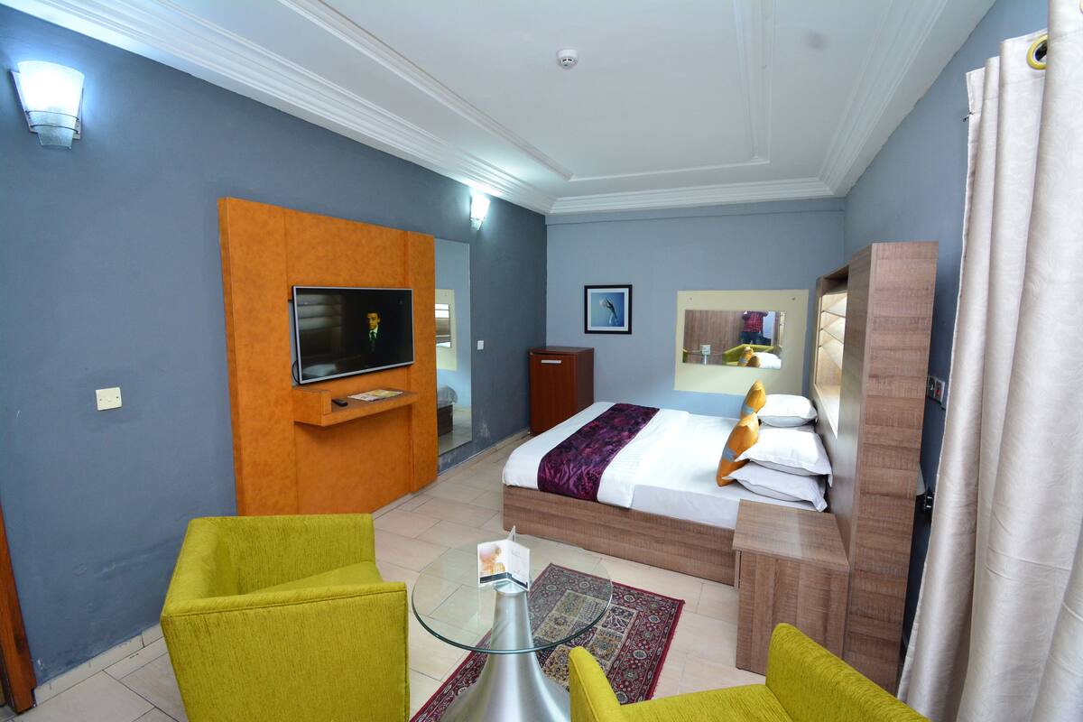 Quarto de hotel com cama, televisão, escrivaninha e duas cadeiras.