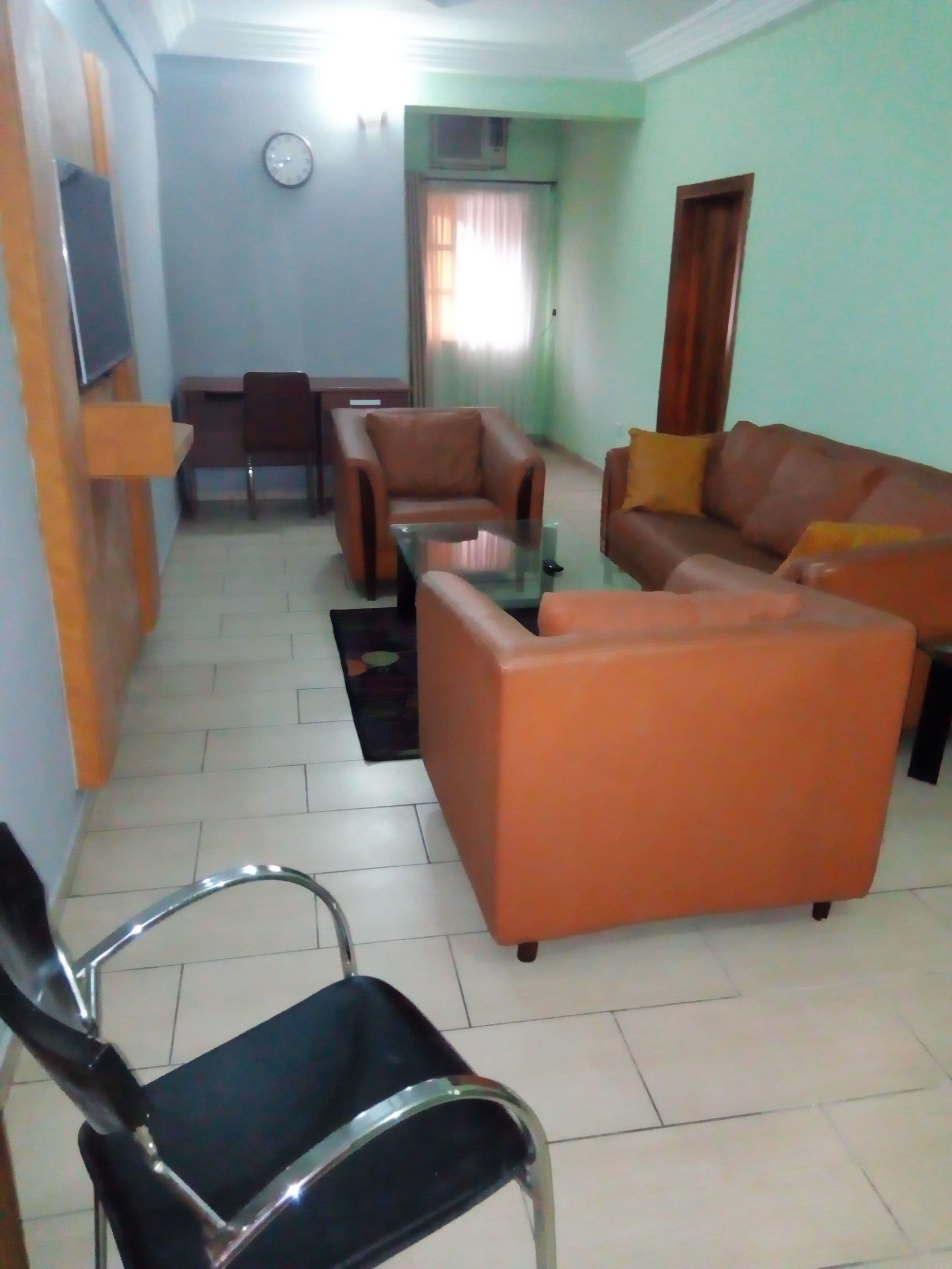A living room with a sofa, armchairs, a coffee table, and a TV mounted on the wall.