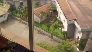 Vista dalla finestra su un cortile con edifici, una zona pavimentata e un paesaggio lontano.